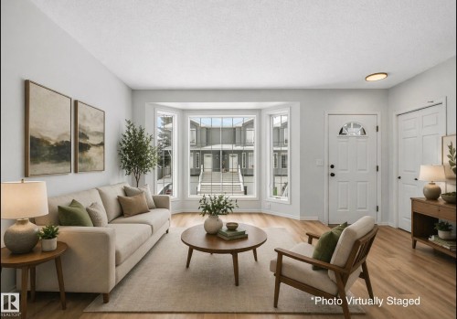 Bright living area featuring wood-finish flooring, a bay window with multiple panes, a white entry door with an arched glass insert, and a double-door closet. Photo Virtually Staged. - 14 15128 22 Street, Edmonton, AB - Indoor Photo Showing Living Room