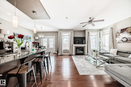 This open-concept interior features rich hardwood flooring, a kitchen island with seating, a fireplace with a mantel, and large windows that provide natural light - 3220 151 Avenue, Edmonton, AB - Indoor Photo Showing Living Room With Fireplace