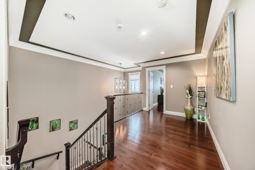 The property features a hallway with rich hardwood flooring, a tray ceiling with recessed lighting, and a staircase with dark wood banisters and metal balusters - 3220 151 Avenue, Edmonton, AB - Indoor Photo Showing Other Room