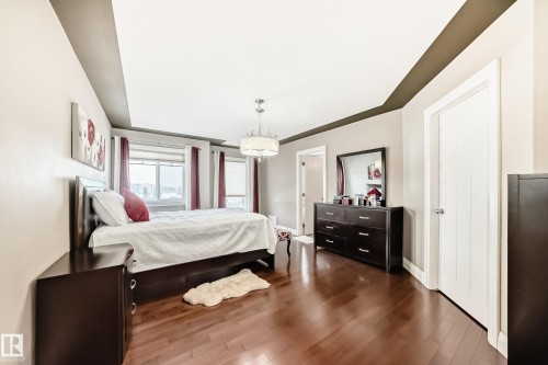 The property features rich hardwood flooring, a tray ceiling with accent trim, and large windows providing natural light - 3220 151 Avenue, Edmonton, AB - Indoor Photo Showing Bedroom