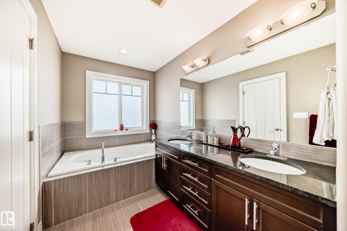 The bathroom features a built-in bathtub with a window, a double vanity with dark wood cabinetry, and a large mirror with integrated lighting - 3220 151 Avenue, Edmonton, AB - Indoor Photo Showing Bathroom