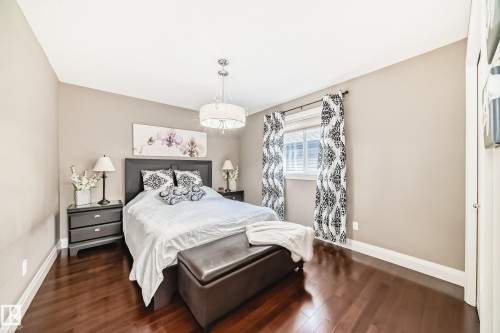 This bedroom features hardwood flooring, a window with white blinds and patterned curtains, and a chandelier-style light fixture - 3220 151 Avenue, Edmonton, AB - Indoor Photo Showing Bedroom