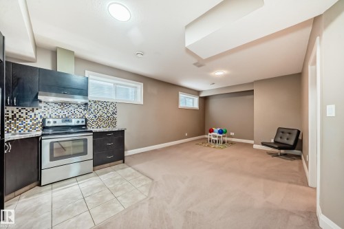 This expansive room offers a full kitchen with dark cabinetry, stainless steel appliances, and a mosaic tile backsplash - 3220 151 Avenue, Edmonton, AB - Indoor