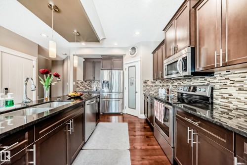 The kitchen features dark wood cabinetry, stainless steel appliances, granite countertops, and a decorative tile backsplash - 3220 151 Avenue, Edmonton, AB - Indoor Photo Showing Kitchen With Stainless Steel Kitchen With Upgraded Kitchen