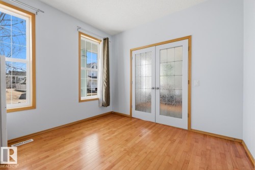 Room featuring wood-finish flooring, two large windows with wood trim, and a pair of French doors with frosted glass panels - 9904 144 Avenue, Edmonton, AB - Indoor Photo Showing Other Room