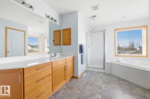 Spacious bathroom featuring a dual vanity with light wood cabinetry, a large mirror, tile flooring, a glass-enclosed shower, and a built-in corner tub - 9904 144 Avenue, Edmonton, AB - Indoor Photo Showing Bathroom