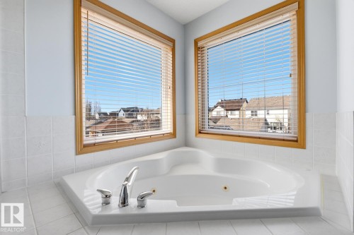 Corner-set jetted tub with chrome fixtures, surrounded by white tiled decking and walls - 9904 144 Avenue, Edmonton, AB - Indoor Photo Showing Bathroom