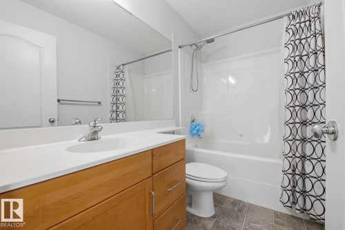 Bathroom featuring a vanity with wood-finish cabinetry and white countertop, an integrated sink with a brushed nickel faucet, a large wall-mounted mirror, and a bathtub with shower - 9904 144 Avenue, Edmonton, AB - Indoor Photo Showing Bathroom