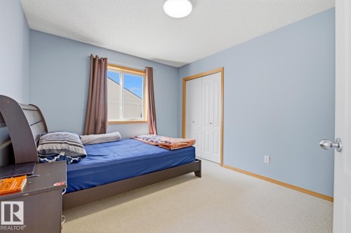 Bedroom featuring a window with a wood frame, light-colored carpeting, a flat ceiling with a flush-mount light fixture, and bifold closet doors with wood trim - 9904 144 Avenue, Edmonton, AB - Indoor Photo Showing Bedroom