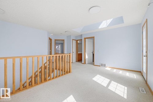 Expansive upper-level space featuring a skylight, light wood railings, light blue walls, and neutral carpet flooring - 9904 144 Avenue, Edmonton, AB - Indoor Photo Showing Other Room