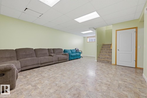 Spacious lower-level room featuring durable tile-patterned flooring, light green walls, and a white drop ceiling with integrated lighting - 9904 144 Avenue, Edmonton, AB - Indoor Photo Showing Other Room