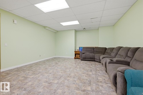 Spacious room featuring light green walls, a grid-patterned ceiling with recessed lighting, and durable tile-look flooring - 9904 144 Avenue, Edmonton, AB - Indoor Photo Showing Basement