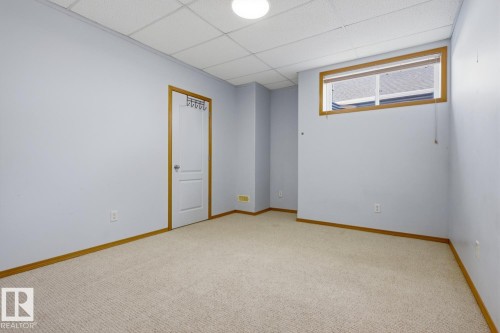 Carpeted room featuring a drop ceiling, a single window with wood trim, and a white interior door with wood trim - 9904 144 Avenue, Edmonton, AB - Indoor Photo Showing Other Room