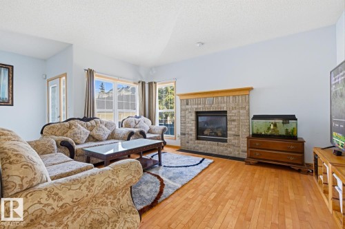 Living area featuring wood-finish flooring, a brick fireplace with a wood mantel, and multiple windows providing natural light - 9904 144 Avenue, Edmonton, AB - Indoor Photo Showing Living Room With Fireplace