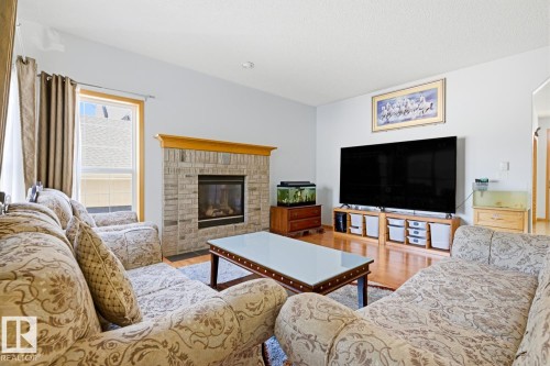 Living area featuring wood-finish flooring, a brick-surround fireplace with wood mantle, and a large window with blinds - 9904 144 Avenue, Edmonton, AB - Indoor Photo Showing Living Room With Fireplace