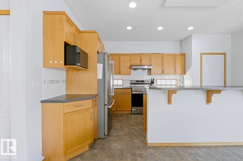 Kitchen featuring wood-finish cabinetry, stainless steel appliances, recessed lighting, and a breakfast bar - 9904 144 Avenue, Edmonton, AB - Indoor Photo Showing Kitchen
