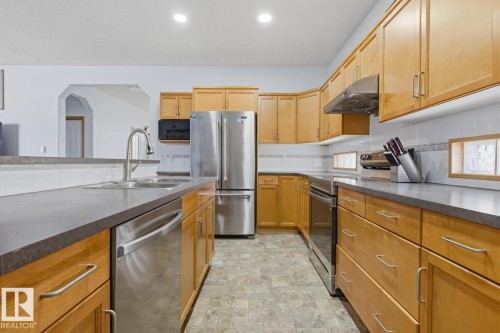 Kitchen featuring extensive light wood cabinetry, stainless steel appliances, dark countertops, and a double basin sink with a pull-down faucet - 9904 144 Avenue, Edmonton, AB - Indoor Photo Showing Kitchen With Double Sink