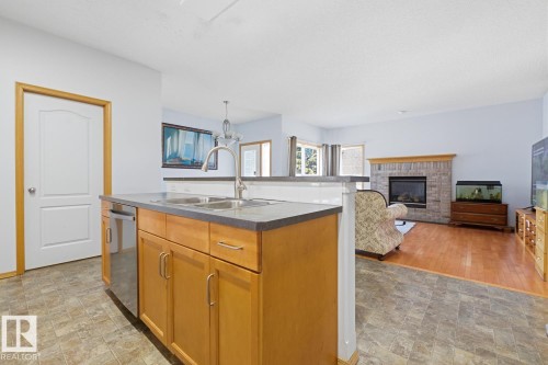 Kitchen island with a double basin stainless steel sink, pull-down faucet, and integrated dishwasher - 9904 144 Avenue, Edmonton, AB - Indoor Photo Showing Kitchen With Fireplace With Double Sink