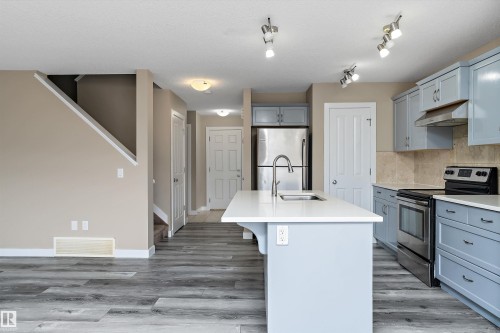Modern kitchen featuring light blue cabinetry, stainless steel appliances, a white countertop island with an undermount sink, and wood-finish flooring - 3314 9 Street Nw, Edmonton, AB - Indoor Photo Showing Kitchen With Upgraded Kitchen