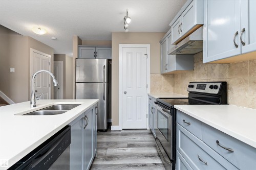 Kitchen featuring light blue cabinetry, white countertops, stainless steel appliances, wood-finish flooring, and a tiled backsplash - 3314 9 Street Nw, Edmonton, AB - Indoor Photo Showing Kitchen With Double Sink With Upgraded Kitchen
