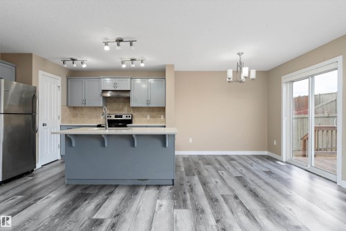 Spacious kitchen and dining area featuring an island with a countertop, stainless steel appliances, light gray cabinetry, and wood-finish flooring - 3314 9 Street Nw, Edmonton, AB - Indoor Photo Showing Kitchen