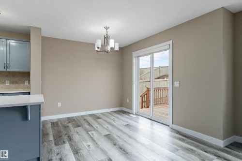 Dining area featuring wood-finish flooring, a contemporary chandelier, a sliding glass door providing access to an outdoor deck, light-toned walls, and white baseboards - 3314 9 Street Nw, Edmonton, AB - Indoor
