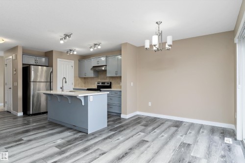 Contemporary kitchen featuring gray cabinetry, stainless steel appliances, a center island with sink, neutral backsplash, and wood-finish flooring - 3314 9 Street Nw, Edmonton, AB - Indoor Photo Showing Kitchen With Upgraded Kitchen