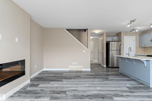 Open-concept living space featuring wood-finish flooring, a modern linear fireplace, a kitchen island with seating, stainless steel appliances, and track lighting - 3314 9 Street Nw, Edmonton, AB - Indoor Photo Showing Kitchen