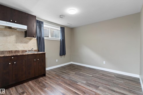 Compact kitchenette featuring dark wood-finish cabinetry, a single basin sink, and a tiled backsplash - 3314 9 Street Nw, Edmonton, AB - Indoor Photo Showing Other Room