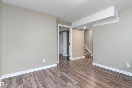 Spacious interior room featuring wood-finish flooring, neutral wall paint, white trim, recessed lighting, and a visible doorway leading to an additional space - 3314 9 Street Nw, Edmonton, AB - Indoor Photo Showing Other Room