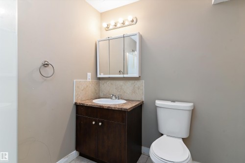 Bathroom vanity featuring a built-in sink, dark wood-finish cabinetry, and a light-toned countertop with a tiled backsplash - 3314 9 Street Nw, Edmonton, AB - Indoor Photo Showing Bathroom