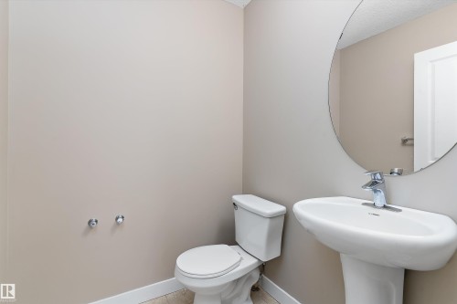 Pedestal sink with chrome faucet, circular wall mirror, and neutral painted walls - 3314 9 Street Nw, Edmonton, AB - Indoor Photo Showing Bathroom