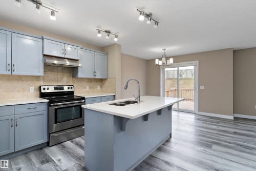 Modern kitchen featuring light blue cabinetry, stainless steel appliances, a center island with a double basin sink, and wood-finish flooring - 3314 9 Street Nw, Edmonton, AB - Indoor Photo Showing Kitchen With Double Sink