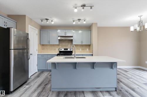 Kitchen featuring an island with a white countertop and seating overhang, light blue cabinetry, stainless steel appliances, and wood-finish flooring - 3314 9 Street Nw, Edmonton, AB - Indoor Photo Showing Kitchen With Upgraded Kitchen
