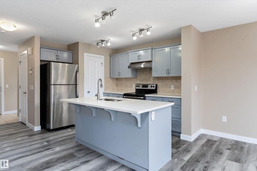 Modern kitchen featuring a central island with a white countertop and integrated sink, stainless steel refrigerator, black range, and blue cabinetry - 3314 9 Street Nw, Edmonton, AB - Indoor Photo Showing Kitchen With Upgraded Kitchen