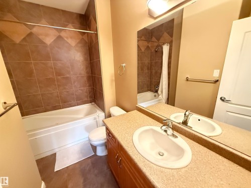 Bathroom featuring a white bathtub with brown tiled surround, a white toilet, and a vanity with a single sink and mirror - 438 1406 Hodgson Way, Edmonton, AB - Indoor Photo Showing Bathroom