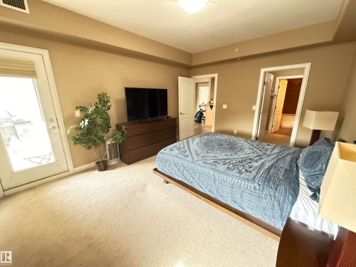 This room features wall-to-wall carpeting, neutral wall colors, and a door leading to a balcony - 438 1406 Hodgson Way, Edmonton, AB - Indoor Photo Showing Bedroom