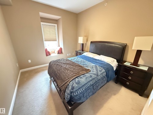 This room features neutral-toned walls and carpeting, a window with a roller blind, and a built-in window seat - 438 1406 Hodgson Way, Edmonton, AB - Indoor Photo Showing Bedroom