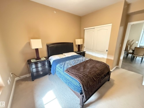 This room features neutral-toned walls, light-colored carpeting, a bed with a dark headboard, and two bedside tables with lamps - 438 1406 Hodgson Way, Edmonton, AB - Indoor Photo Showing Bedroom
