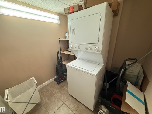 Dedicated laundry area featuring a stacked washer and dryer unit, tiled flooring, and overhead lighting - 438 1406 Hodgson Way, Edmonton, AB - Indoor Photo Showing Laundry Room