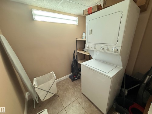 Laundry area featuring a stacked washer and dryer, tile flooring, and a fluorescent light fixture - 438 1406 Hodgson Way, Edmonton, AB - Indoor Photo Showing Laundry Room