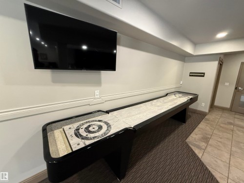 Entertainment space featuring a large wall-mounted television, a shuffleboard table with a target design, and a combination of carpet and tiled flooring - 438 1406 Hodgson Way, Edmonton, AB - Indoor Photo Showing Other Room