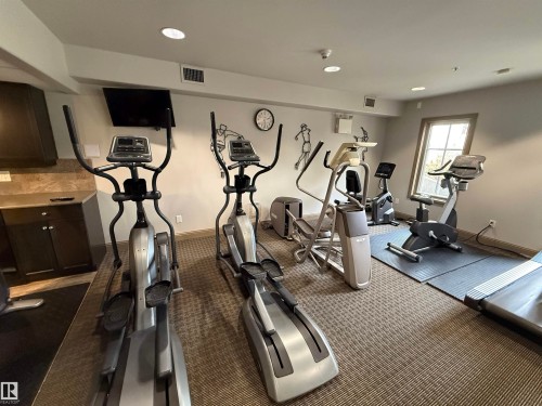 The property includes a fitness area featuring various exercise machines, recessed lighting, and a window providing natural light - 438 1406 Hodgson Way, Edmonton, AB - Indoor Photo Showing Gym Room
