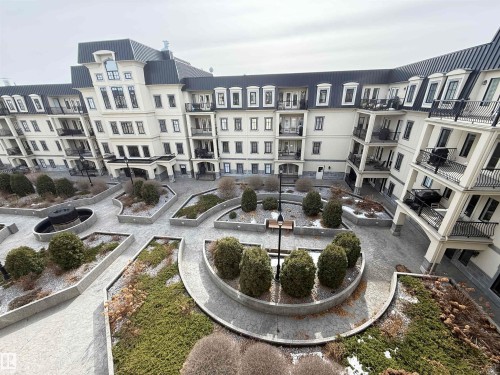 The property offers a courtyard with structured landscaping, featuring various plantings within raised beds and paved walkways - 438 1406 Hodgson Way, Edmonton, AB - Outdoor With Facade