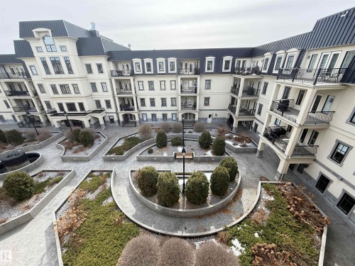 The property features an inner courtyard with landscaped garden beds, paved walkways, and a contemporary architectural style with balconies - 438 1406 Hodgson Way, Edmonton, AB - Outdoor With Facade