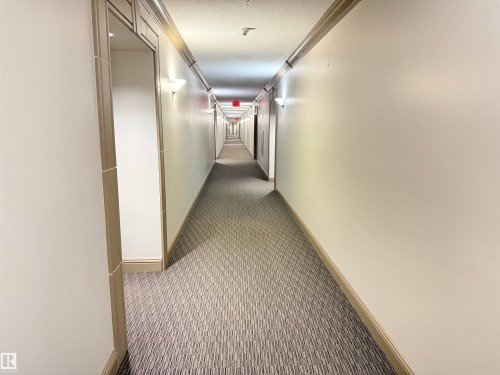 A well-lit hallway featuring wall sconces and carpeted flooring - 438 1406 Hodgson Way, Edmonton, AB - Indoor Photo Showing Other Room