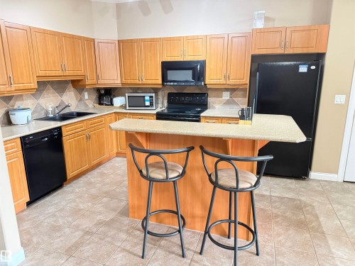 The kitchen features tile flooring, light wood cabinetry, and a countertop with an integrated breakfast bar - 438 1406 Hodgson Way, Edmonton, AB - Indoor Photo Showing Kitchen With Double Sink