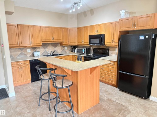 The kitchen features light wood cabinetry, a tiled backsplash, and black appliances - 438 1406 Hodgson Way, Edmonton, AB - Indoor Photo Showing Kitchen