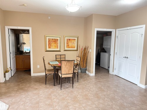 The property features tile flooring throughout, a dining area with a round table and four chairs, and a utility area with a stacked washer and dryer - 438 1406 Hodgson Way, Edmonton, AB - Indoor