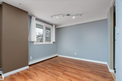 Room featuring wood-finish flooring, a window with white trim, track lighting, and a baseboard heating unit - 206 9929 113 Street, Edmonton, AB - Indoor Photo Showing Other Room